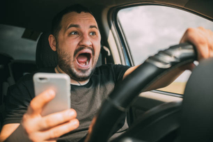 Young man sitting in his car screaming distracted by smartphone texting