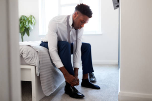 Businessman At Home Sitting On Bed Putting On Shoes Before Leaving For Work