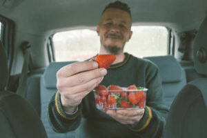 Adult man taking one delicious strawberry from fruit plastic container. PET, or Polyethylene Terephthalate container.