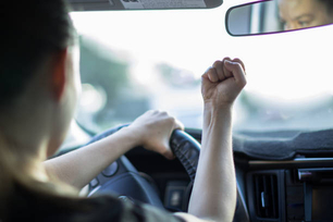 A angry adult sitting in the car, holding a fist up at another driver.
