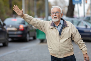 An Older Man is Rushing to the Work Place. A Bearded Man with Eyeglasses is Standing in the Street and Hailing for a Taxi with Raised Arm.