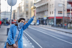 A Woman With a Protective Face Mask is Rushing to the Work Place. Young Woman is Standing in the Street and Hailing for a Taxi with Raised Arm During a Corona Virus Time.
