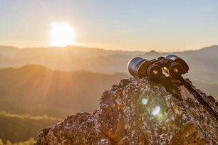 binoculars on top of rock mountain at beautiful sunset background.