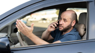 Man sitting in car with mobile phone calling while driving. Distracted shocked guy not paying attention at road using smartphone annoyed by bad news outdoors background