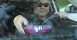 A driver wearing sunglasses placing his Lyft amp on his car's dashboard