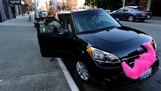 A picture of a black Lyft car with a pink mustache on the front of the vehicle.