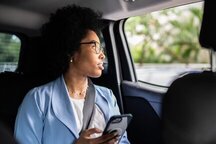 Black woman sitting in the backseat of a car holding her phone looking out the window.