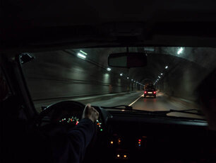 View inside car moving in road tunnel. Hand of man on steering wheel driving automobile