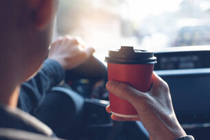 Man driver hand holding takeaway paper coffee cup while driving a car in the morning, close up, toned image