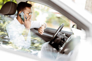 A businessman talks on the phone and looks at his watch while driving a car