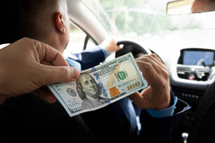 Passengers pay service fees to male taxi drivers. client pays for the trip in dollars. 100 dollar bill in a male hand