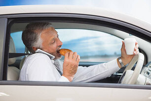 Man drinking coffee and eating donut on phone in his car