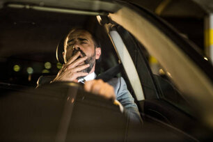 Close-up of overworked mid adult businessman yawning while driving his car back home at night.