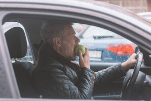 Adult man is eating apple while drive car in the city streets