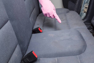 Man's hand in rubber protective glove with finger pointing to dirty textile back seat. Car's interior problem and solution. Cleaning concept.