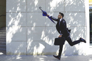 Businessman with umbrella running to catch taxi or bus