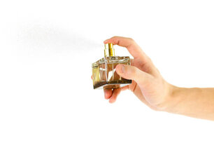 The hand holding the Cologne. Sprays perfume. Isolated on a white background. Close up.